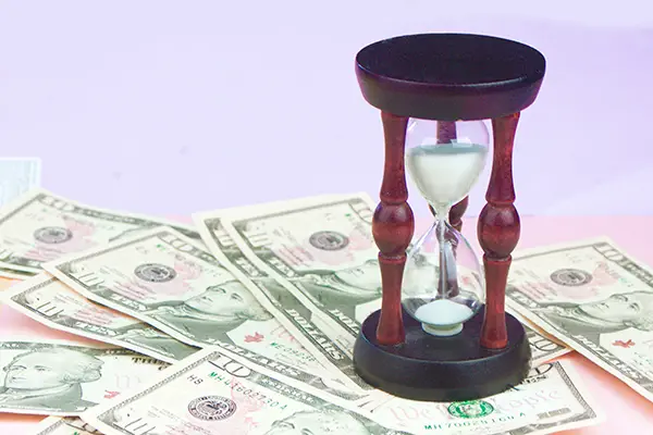 Hourglass on dollar bills representing the time and money businesses save by outsourcing bookkeeping to a trusted professional like Mezzo Financial.